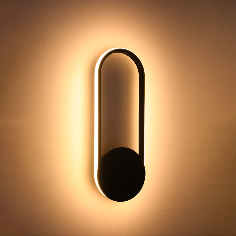 Aplique de pared LED en forma de óvalo negro, ideal para espacios modernos como salas o pasillos, brindando luz ambiental cálida.