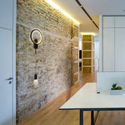 Aplique de pared cosmoring dual con luz cálida, ideal para salas modernas o contemporáneas, añadiendo estilo y funcionalidad.