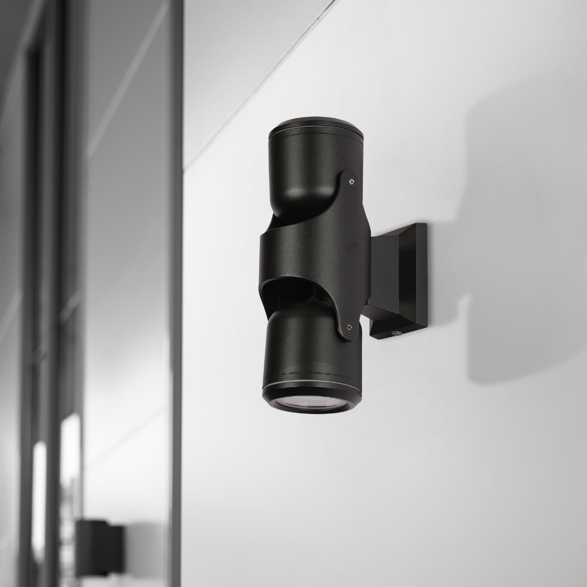 Luz de pared exterior tiltable negra, ideal para patios modernos, iluminando paredes con un estilo contemporáneo.